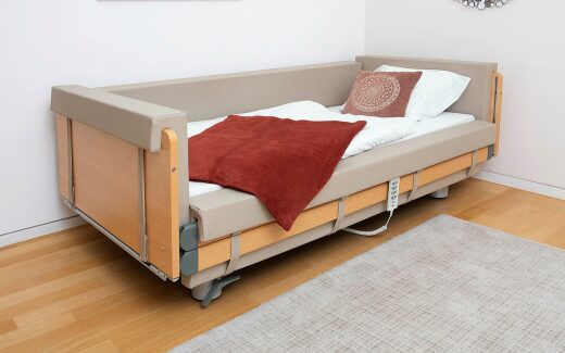 Pflegebett Regia gardo von Burmeier im Zimmer, rundum gepolstert in Beige mit roter Decke